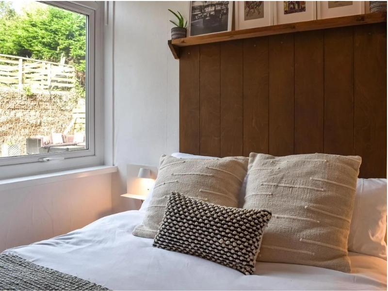 Photo of a cosy double bed with panelled headboard next to a window